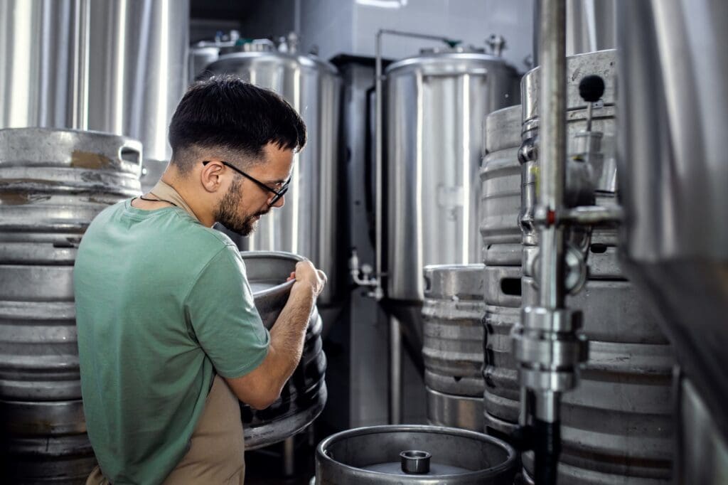 Man working in craft brewery carrying metal barrel.